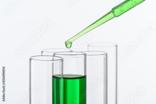 Photos Laboratory dropper transferring green liquid sample into test tubes for chemistry research, pharmaceutical testing, and healthcare scientific experiments with copy space
