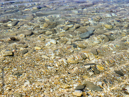 Clear Shallow Water Over Pebble Beach With Gentle Ripples And Sunlit Stones At Shoreline