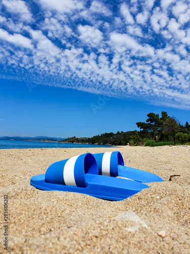 Blue Sandals on Sandy Beach Under Dramatic Cloudscape With Distant Coastline and Summer Vibes