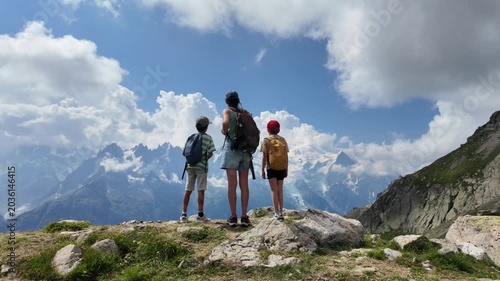 Adventurous mother with her two sons enjoying a scenic view of the mont blanc massif from a mountain top during a family hiking trip in the stunning french alps