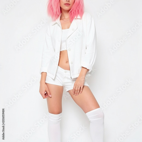 Gen Z youth fashion portrait of a beautiful woman with pink bob haircut in white denim shorts and sports top.