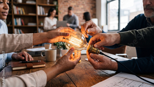 Diverse business team collaborating on a creative project holding a glowing light bulb together