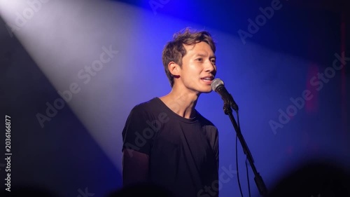 Young man singing passionately into a microphone on a stage with blue spotlights
