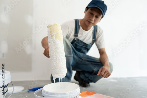 Photos painter man, brush in hand dip on paint for restore and paint the wall, indoor t