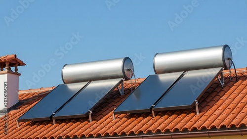Solar panels installed on red tiled rooftop under clear blue sky for renewable energy