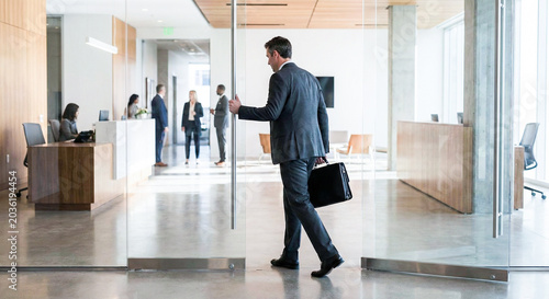 Successful man in business suit entering through glass office door.