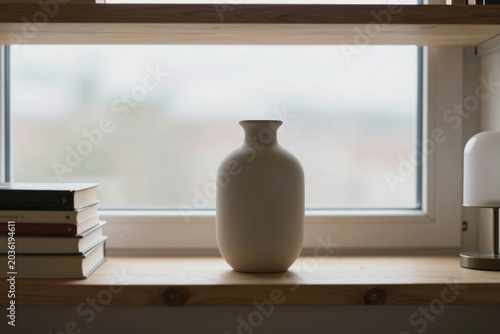 Ceramic matte vase stands and a stack of books on a wooden shelf  in front of a window. Minimalist interior design lifestyle concept.