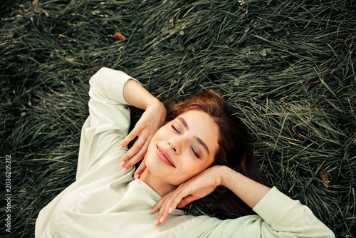 Young woman relaxing on grass with eyes closed  smiling peacefully and enjoying nature and sunlight in a calm outdoor moment