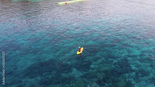 Aerial view of a woman relaxing on a yellow kayak over a beautiful coral reef in crystal clear turquoise sea water background