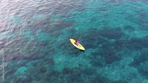 Aerial view of a woman relaxing on a yellow kayak over a beautiful coral reef in crystal clear turquoise sea water background