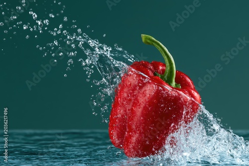 Red pepper splashes with water against a dark green background