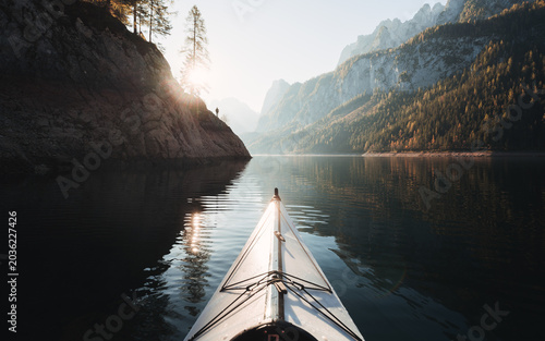 Kayaking on Gosausee lake with person standing one rocks against Dachstein mountain in the background at sunrise, Gosau, Salzkammergut region, Upper Austria, Austria	