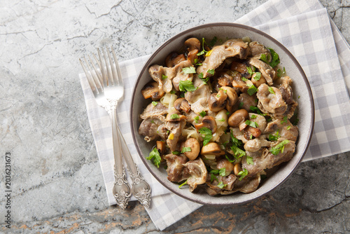 Fotografi Stir-fried chicken giblets with mushrooms and onions close-up in a bowl on the table