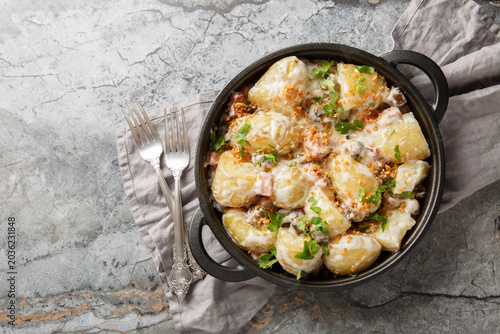 Delicious young potatoes in a creamy mushroom sauce with bacon sprinkled with breadcrumbs and parsley close-up in a frying pan on the table. Horizontal top view from above