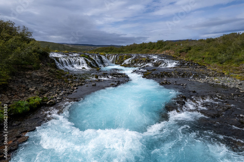Stunning view of the Bruarfoss blue waterfall in Iceland, with turquoise water cascading over rocky terrain. Landscape of a tourist attraction and amazing travel destination.
