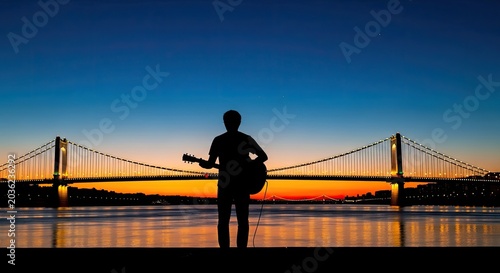 Silhouette of a person with guitar standing in front of a suspension bridge