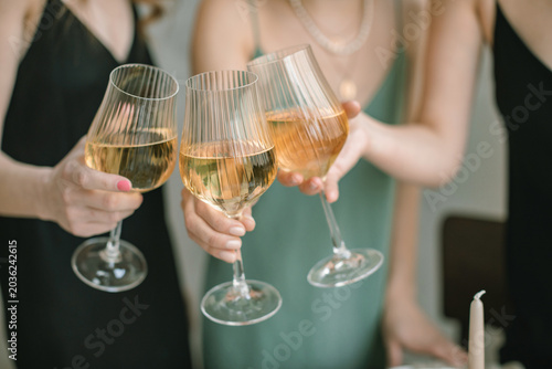 Close-up of three women in party dresses making a celebratory toast with glasses of white wine