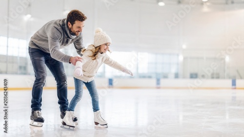 A young girl and an adult man rollerblading in a brightly lit indoor rink family winter sports promotion