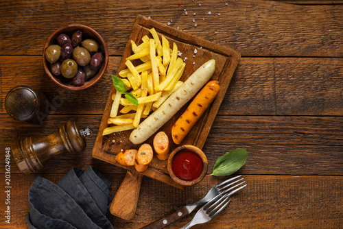 Grilled sausages and french fries on wooden background top view copy space. Fast food