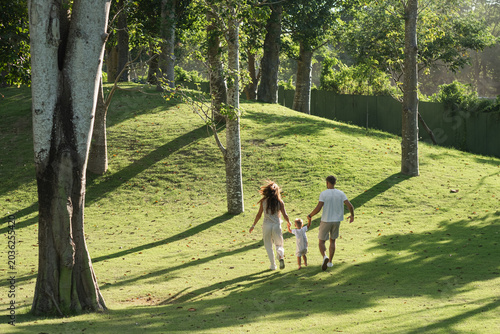 Parents and child walking on green tropical lawn.