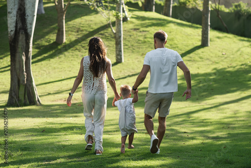 Young family with toddler walking through sunny park.