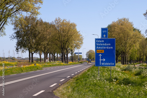 Blue traffic sign along the provincial road N247 near Middelie in North Holland, the Netherlands. The sign indicates the route to local destinations such as Edam, Volendam, Middelie, and Amsterdam.