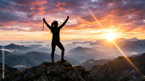 Silhouette of a woman cheering with raised arms on a mountain peak at sunset. This powerful image represents personal achievement, victory, freedom, and reaching a life goal.
