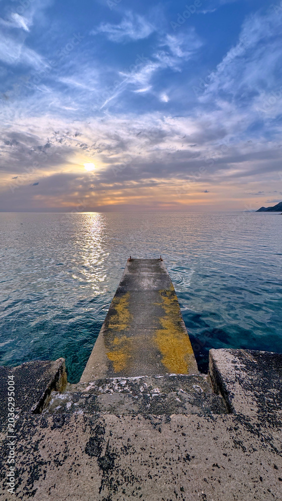 Obraz premium Dobra Voda pier on Adriatic coast at sunset with calm sea and moody sky