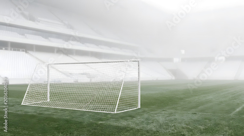 A soccer goal stands alone on a green field in a large stadium with a hazy atmosphere