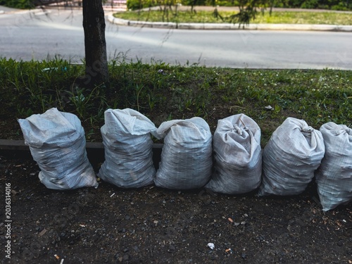 Photos White bags lined up on urban street for waste collection near trees