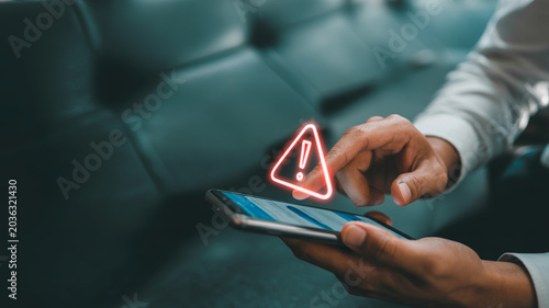 Hand holding smartphone with glowing red warning triangle icon overlay signifying danger or alert on screen.