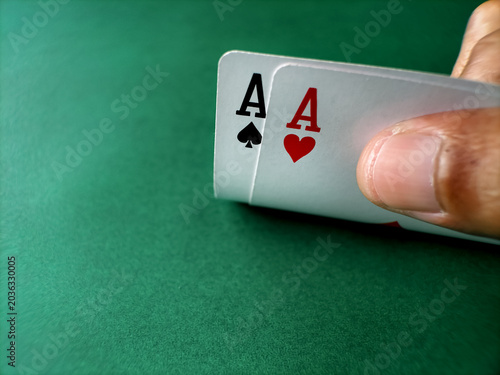Close-up of a poker player holding a pair of aces over a green felt table.