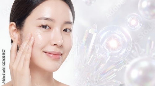 Portrait of Beautiful Young Asian Woman with Perfect Glowing Skin Applying Skincare Gel, Next to Crystals and Luminous Spheres, White Background
