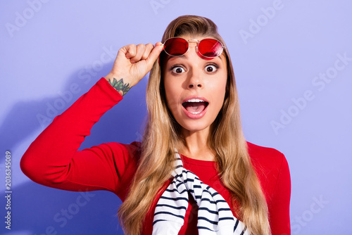 Принти на полотні Surprised young woman in red top lifting red sunglasses to reveal wide-eyed expr