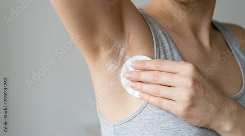 Woman applying antiperspirant to underarm with cotton pad