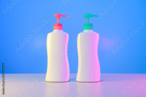 Object Series : Two white pump bottles with colorful pumps stand against a blue background bathed in neon light.