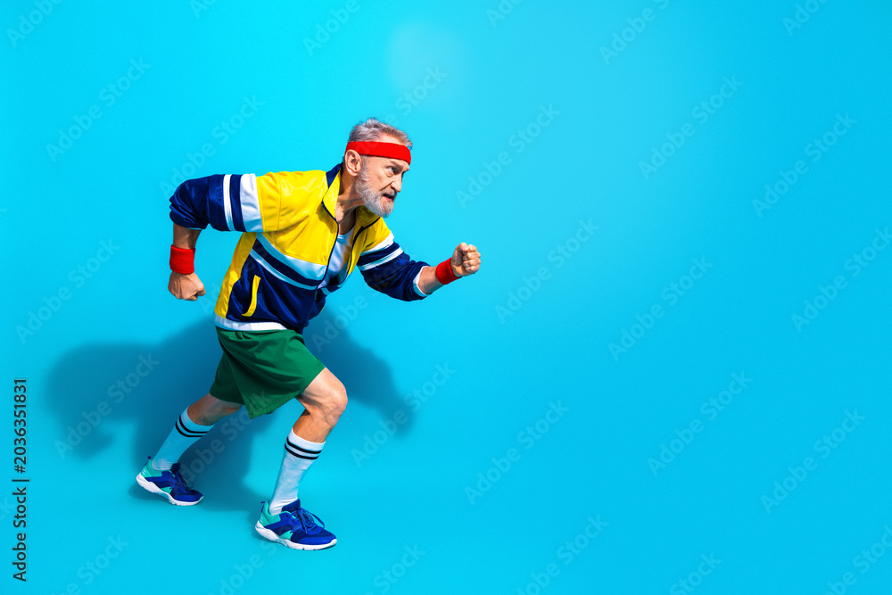 Naklejka premium Senior man sprinting in retro sportswear on bright blue background showing active lifestyle, fitness, energy and playful vintage workout style