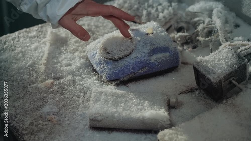 Gloved hand reaching frostcovered telephone on snowdusted desk among scattered papers and ruined electronics, cold blue handset halfburied under crystalline powder, careful inspection for last