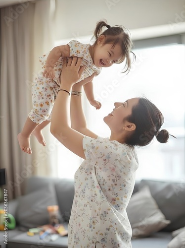 Happy Asian Mother Lifting Toddler Daughter in Floral Outfits - Joyful Family Bonding - Vertical Portrait Stock Photo