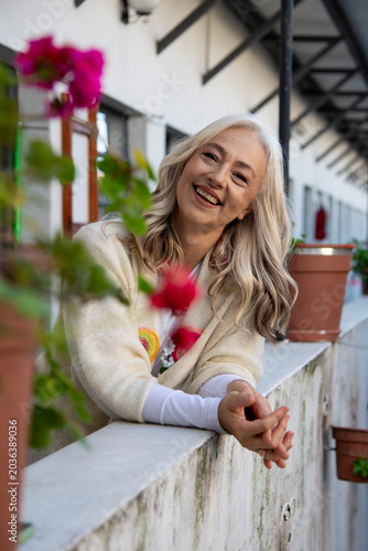Smiling mature woman leaning on balcony with pink flowers