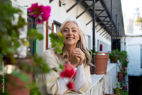 Smiling mature woman leaning on balcony with pink flowers