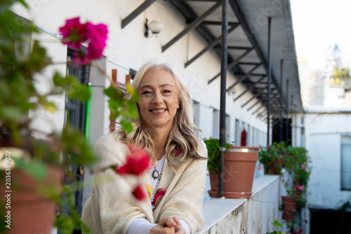 Smiling mature woman leaning on balcony with pink flowers