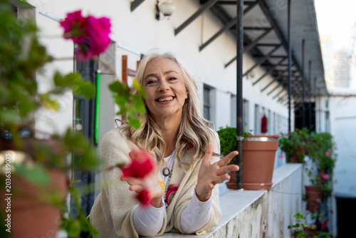 Smiling mature woman leaning on balcony with pink flowers