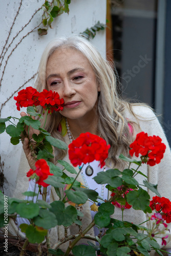 Serene mature woman smelling red flowers with eyes closed