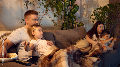 Cuadro en lienzo Cozy family relaxing under blanket while watching movie together in living room