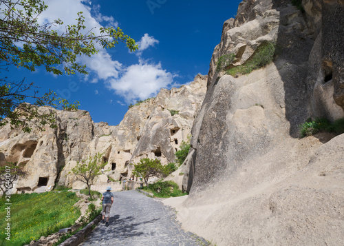 Scenic spring landscape in Göreme, Cappadocia, Türkiye, with fairy chimney rock formations, green hills and wild vegetation under a bright blue sky with white clouds.