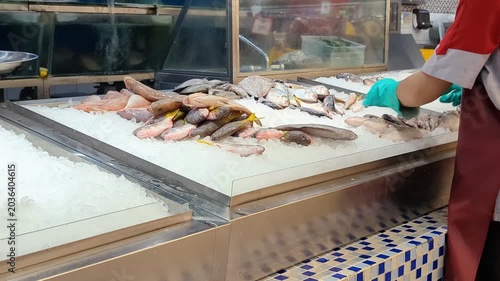 A unrecognisable supermarket employee wearing gloves arranges products on an ice-filled display table, maintaining freshness and an attractive presentation.