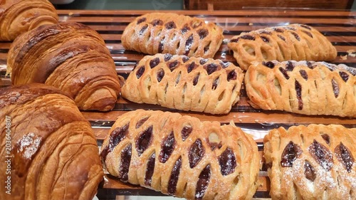 Freshly baked croissants and fruit-filled pastries are neatly displayed on a wooden tray, showcasing golden layers, flaky textures, and a tempting bakery selection.
