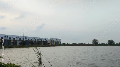 A calm pond view with modern buildings under a cloudy sky, creating a peaceful atmosphere with soft light and gentle water ripples.