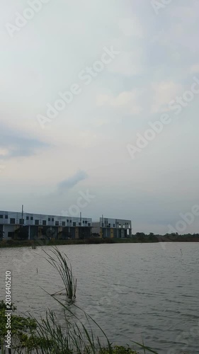 A calm pond view with modern buildings under a cloudy sky, creating a peaceful atmosphere with soft light and gentle water ripples.